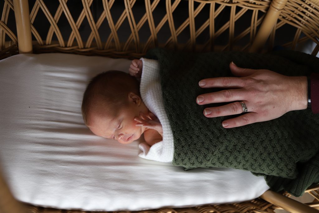 lifestyle newborn example baby snuggled wicker bassinet mums hand