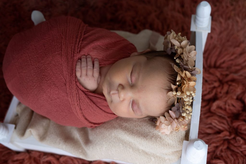 posed studio newborn example red bed wrapped flower crown
